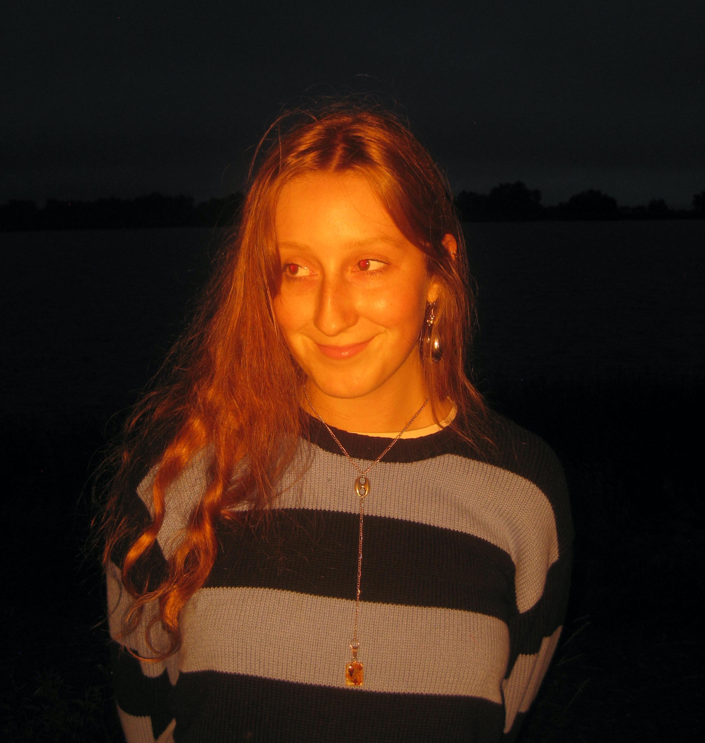 Photo of Olivia MacLeod. The background is dark and she is lit up by a red hue. She's smiling softly, looking in another direction.