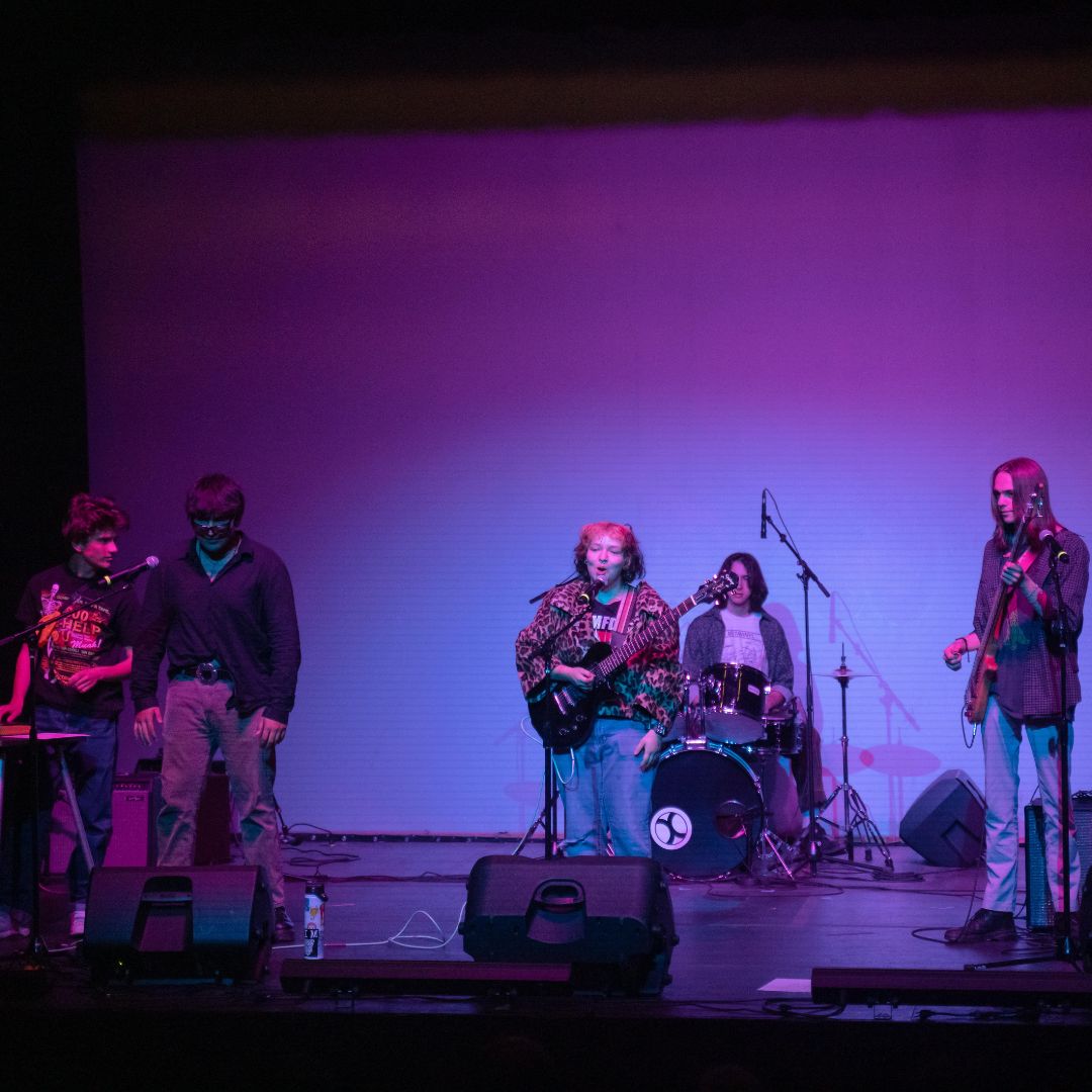 Five piece band performing on a stage.