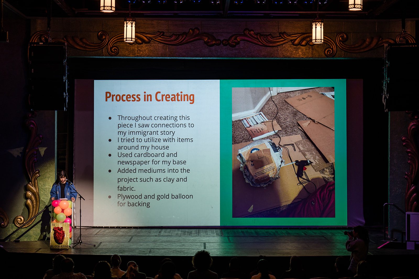 Student presenting on a stage in front of a screen that reads, "process of creating"