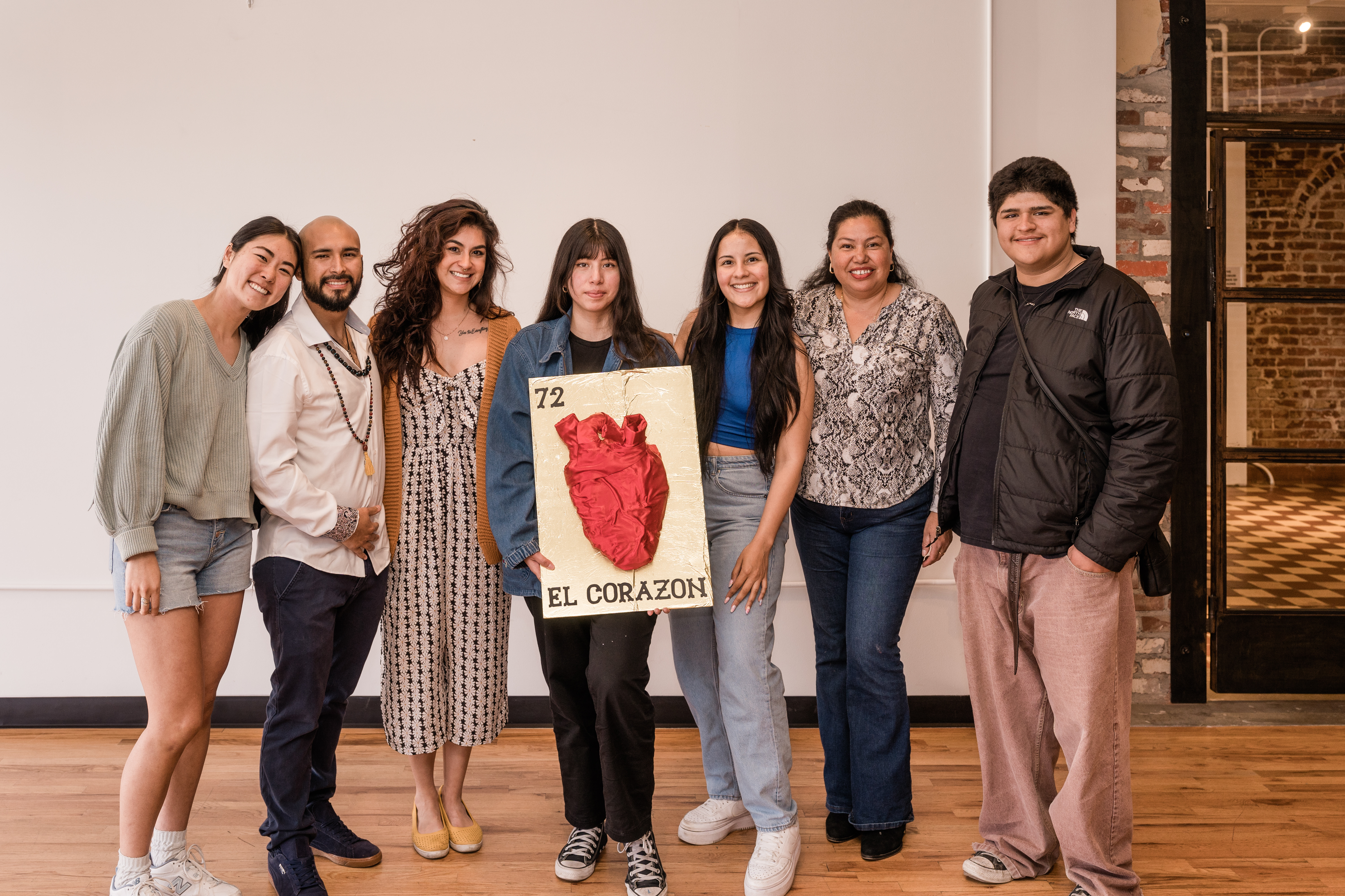 a photo of a young woman and her family. she is holding a crafted heart on a gold background called El Corazon