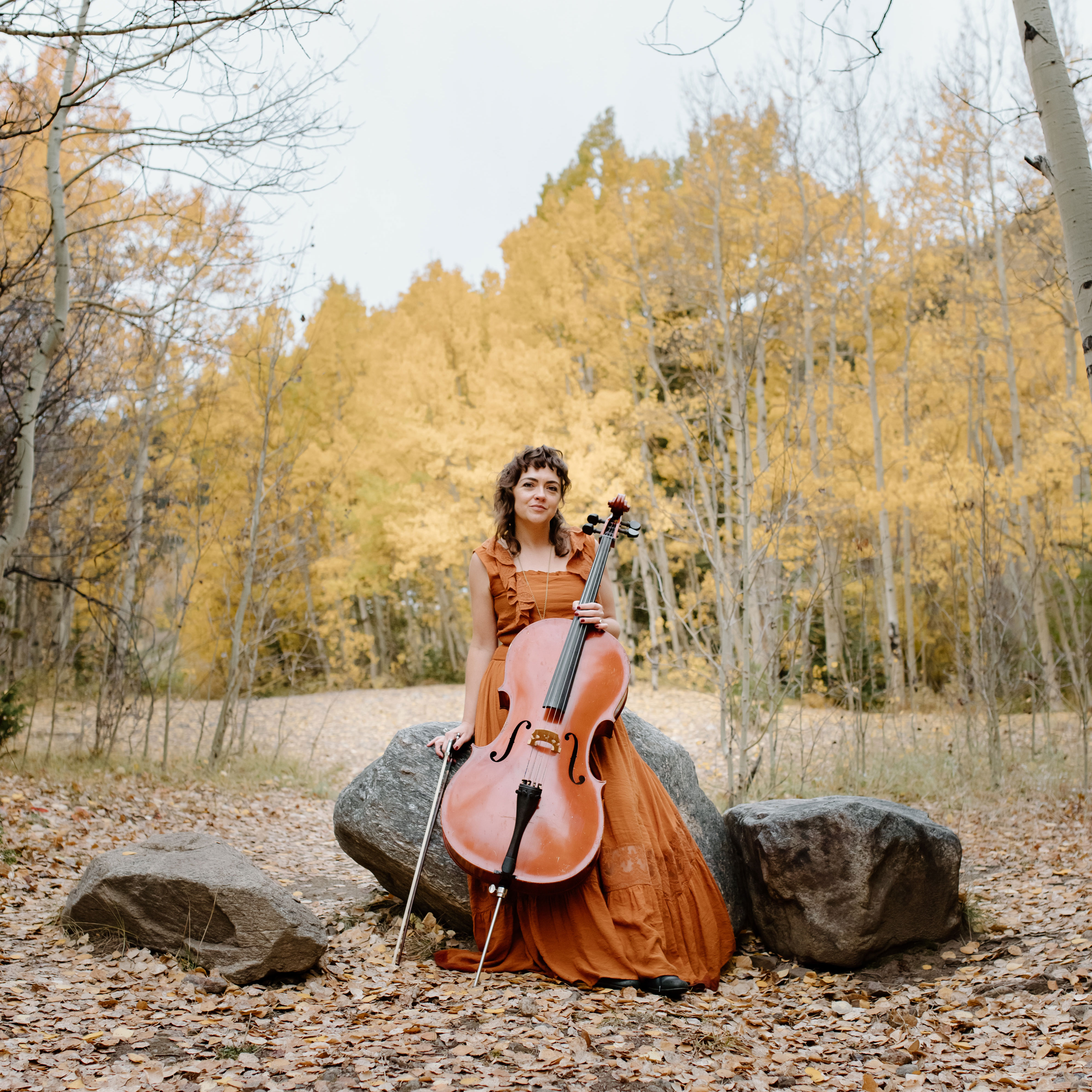 Neyla Pekarek playing a cello in front of aspen trees.