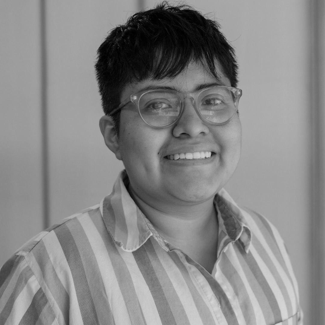 Black and white portrait of a person named Celi Torres, sporting a short hair cut, striped button down, and glasses.