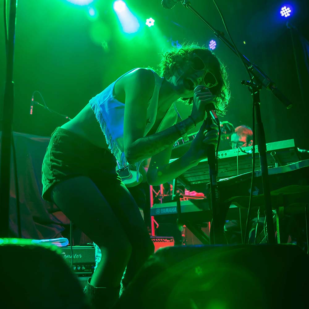 Band photo featuring a person singing on a stage under a hue of green light.