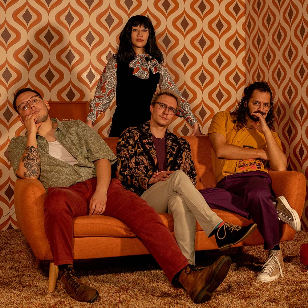 Band photo featuring four people posing in a retro room.