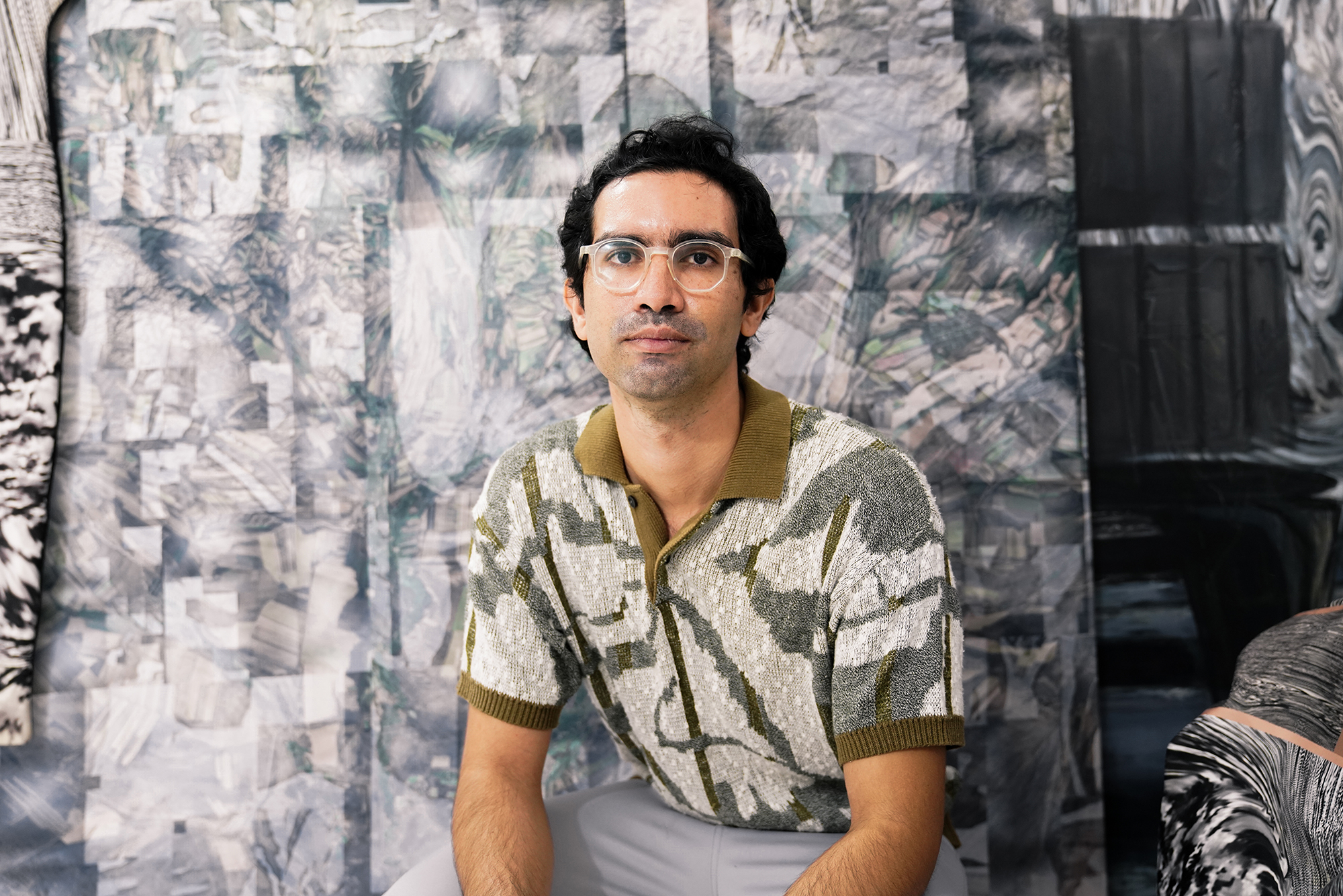 Image of artist Leo Castañeda in an olive great and beige patterned short sleeved button down shirt, against a great  