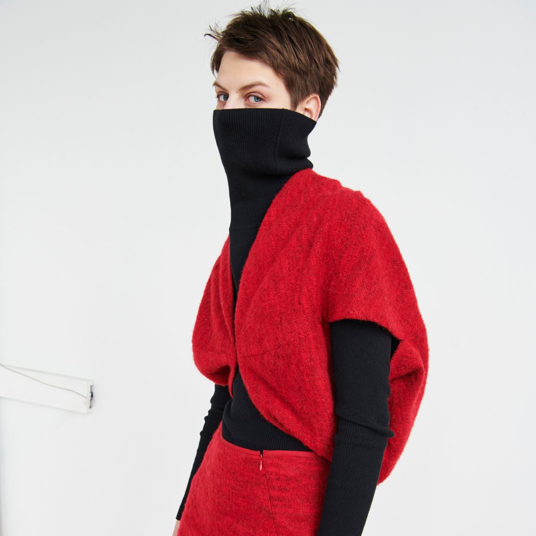 Model wearing a red outfit and a black turtleneck which covers the bottom half of their face. 