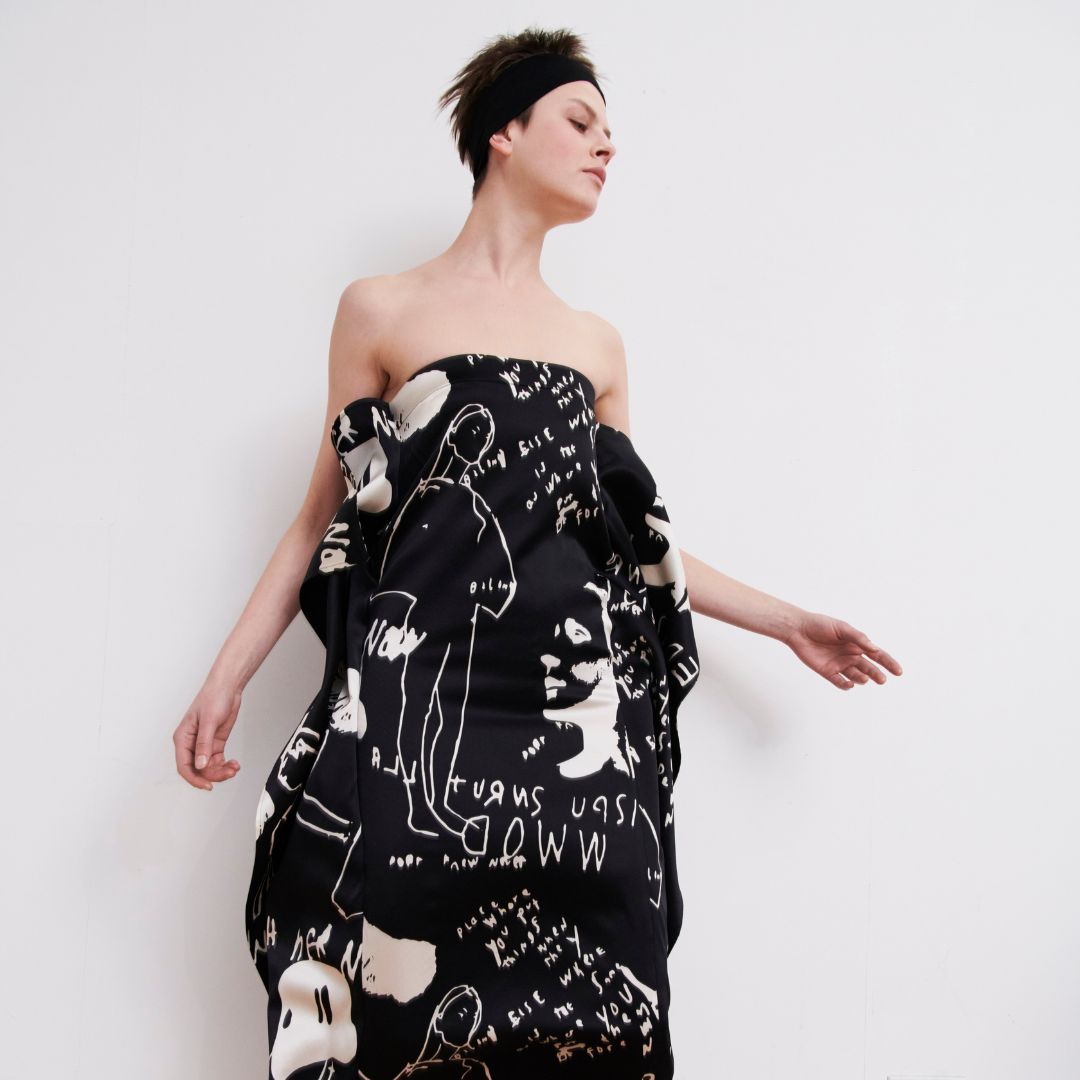 Model wearing a black dress with a white abstract line drawing on it. 