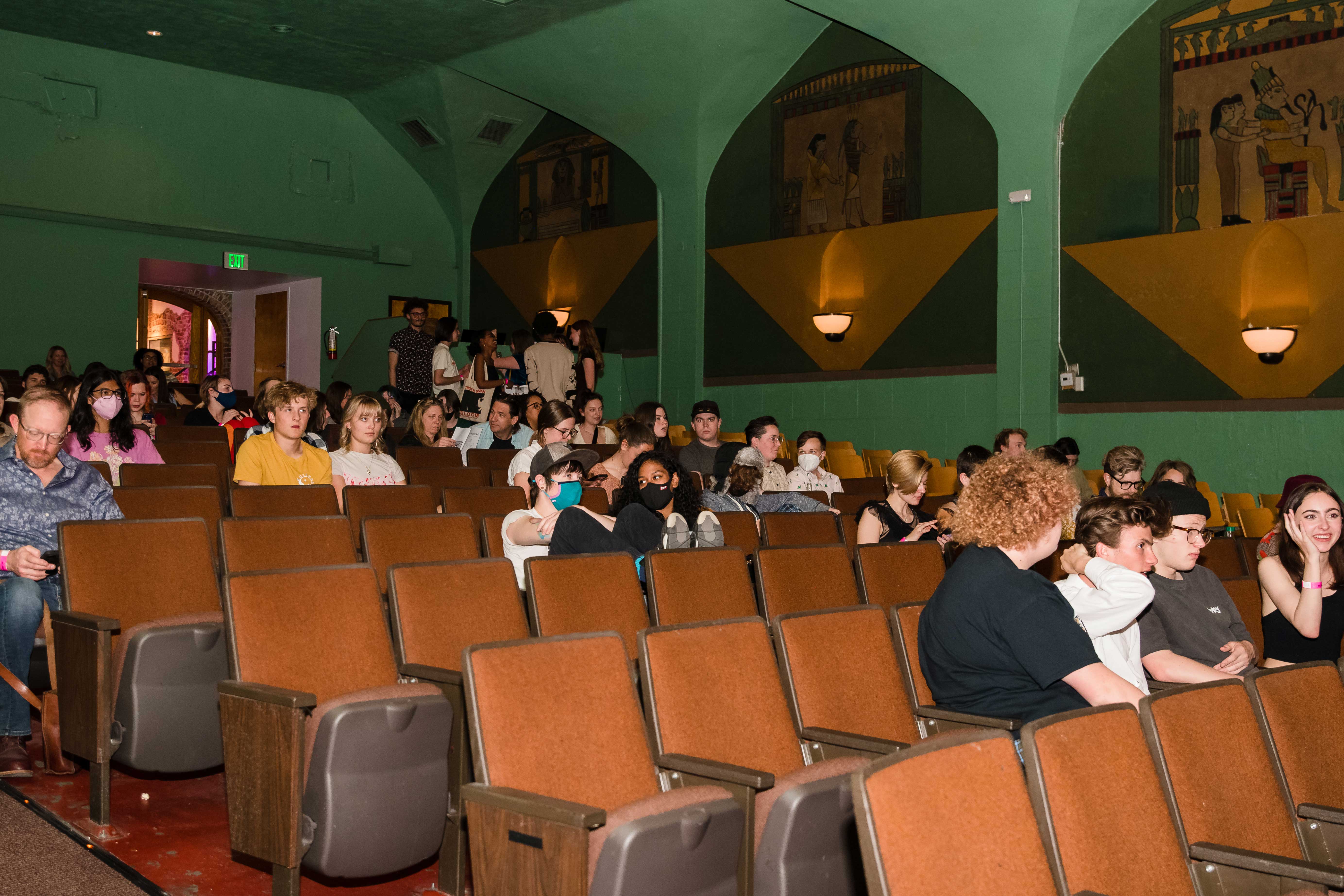 Theater will Egyptian motifs on the walls and people sitting in rows of stacked chairs.