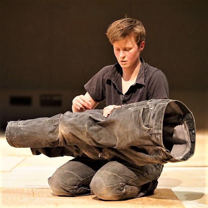 Artist and performer LA Samuelson sitting on the ground holding a pair of stiff black pants.