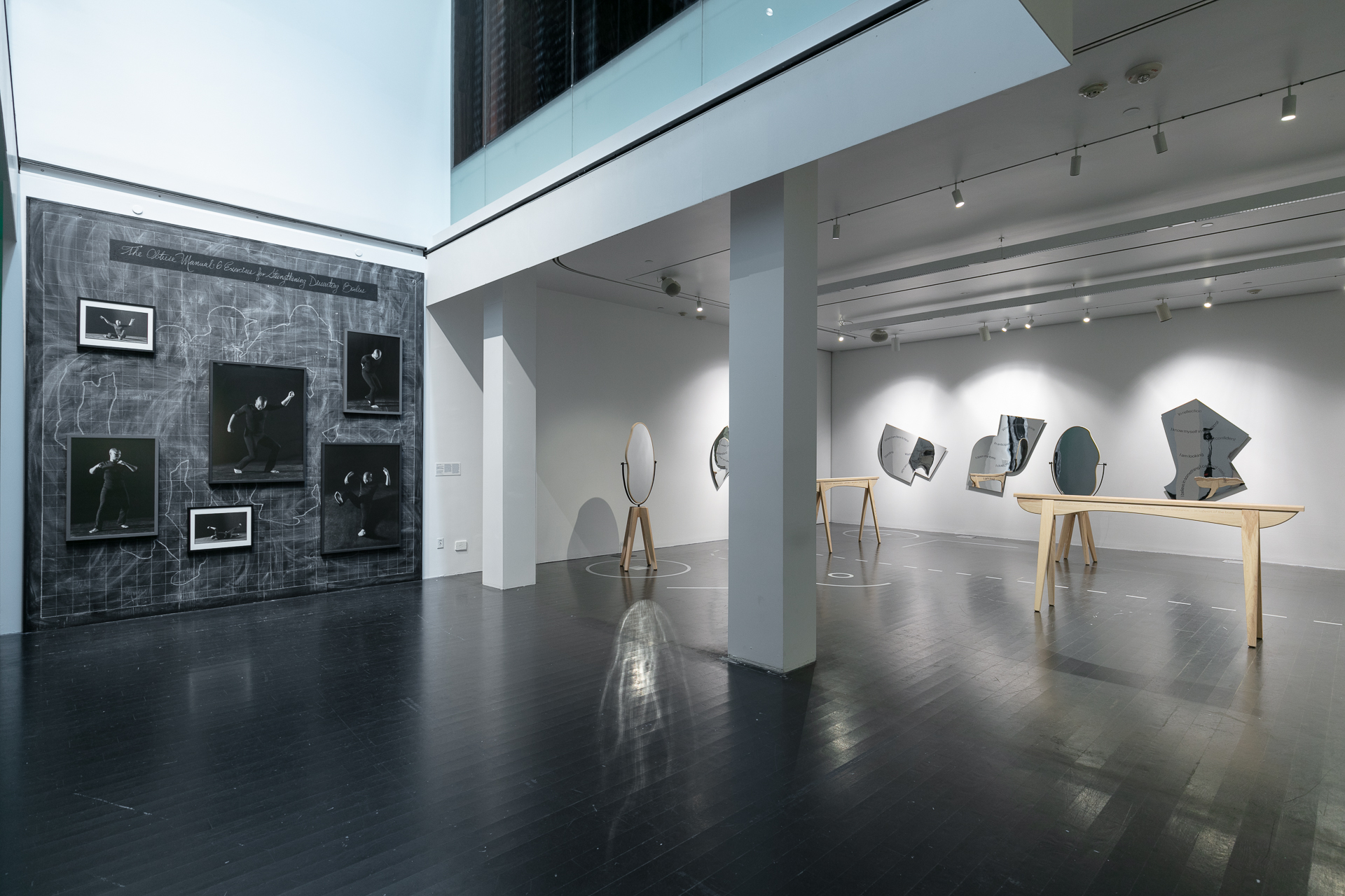 Gallery featuring black and white images hung on the wall and what looks like a ballet or dance studio installation.