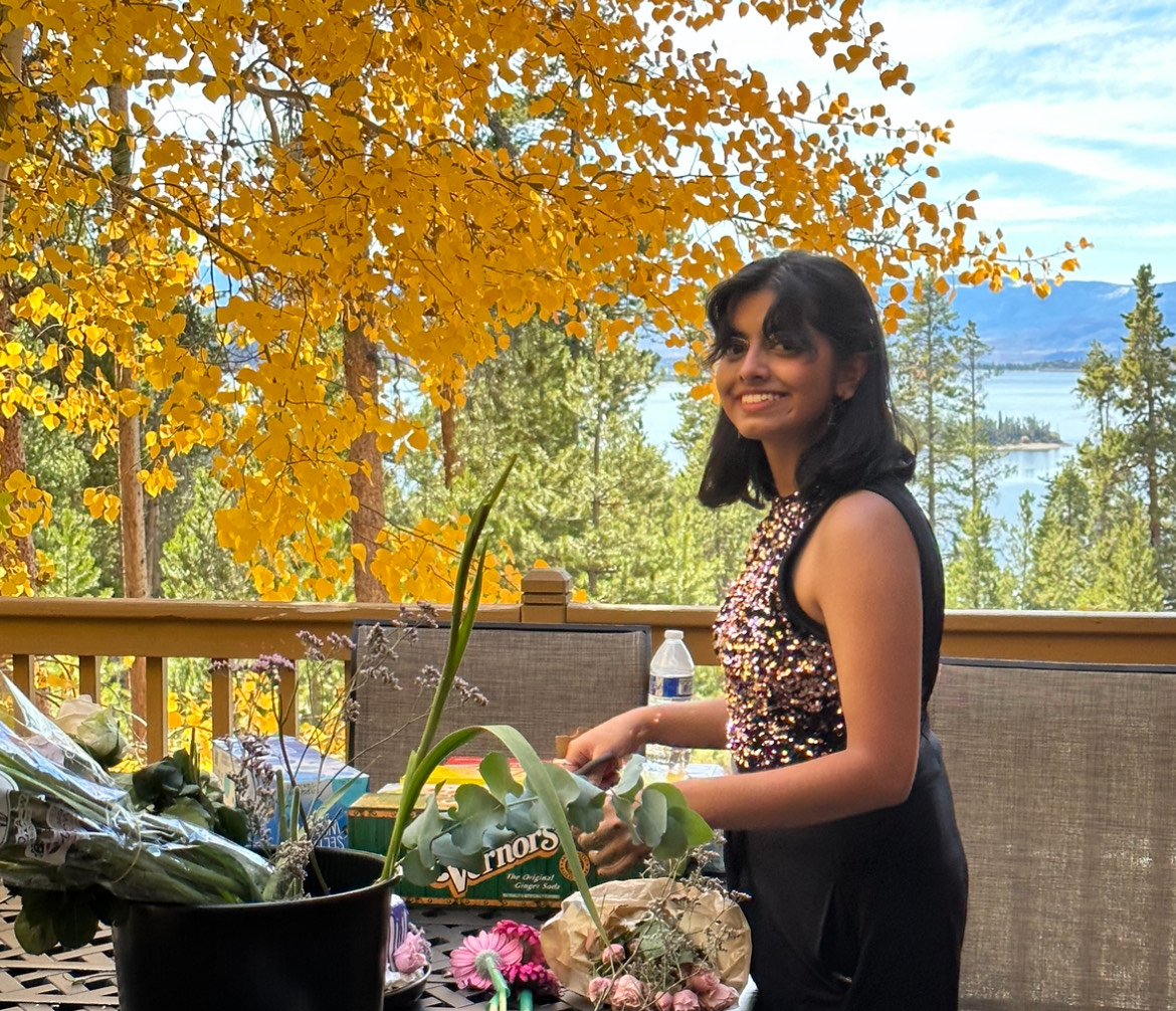 Teen Devaki Sawant smiling outside in front of a yellow aspen tree.
