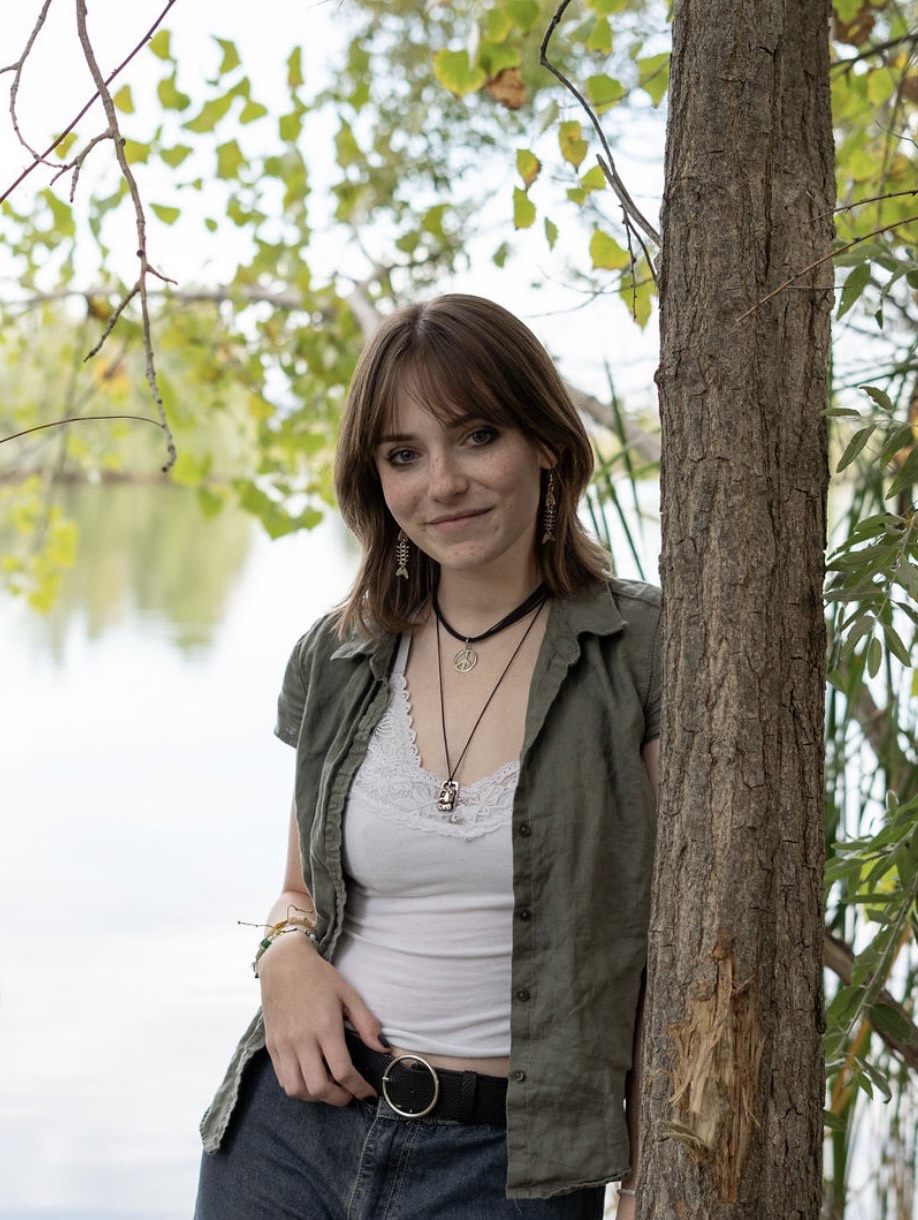 Teen Erin Galimanis smiling softly and posing leaning up against a tree.
