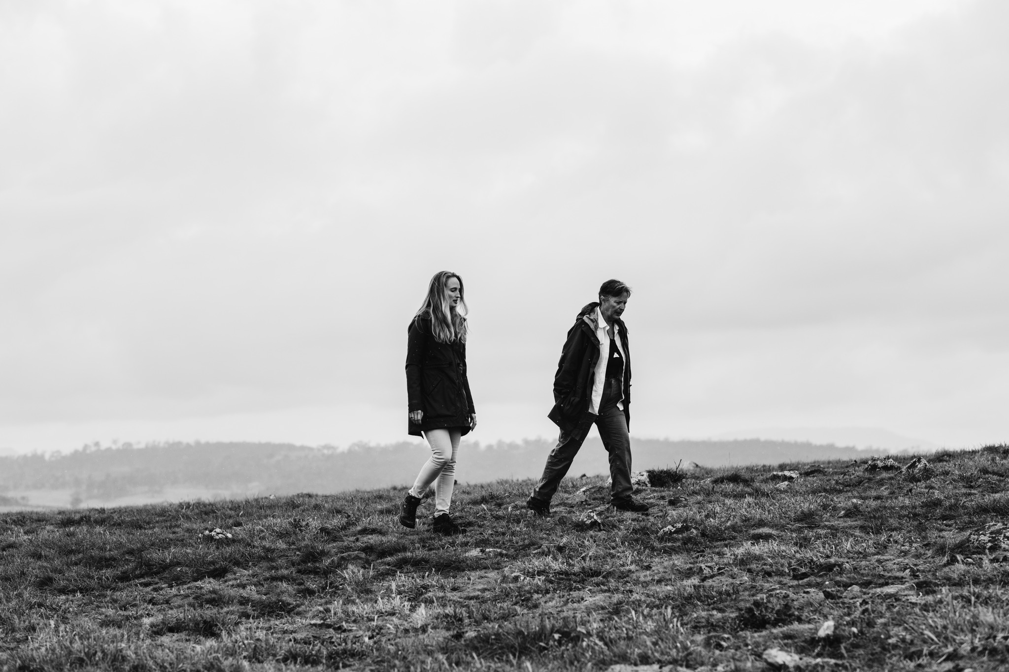 Black and white image featuring two people walking in a scenic landscape.