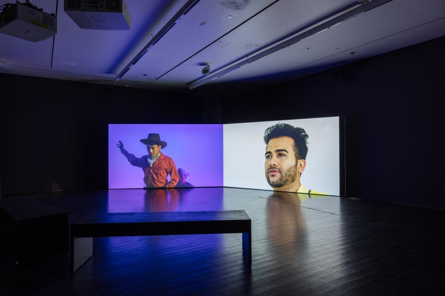 Gallery featuring two-channel video. One screen features a cowboy, the other features a close up of a person's face.