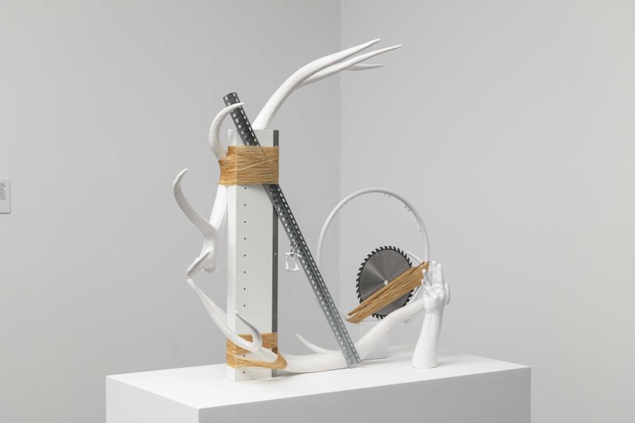 Monochromatic sculpture made of mixed materials. Among them is a plaster cast of a hand and a white antler.