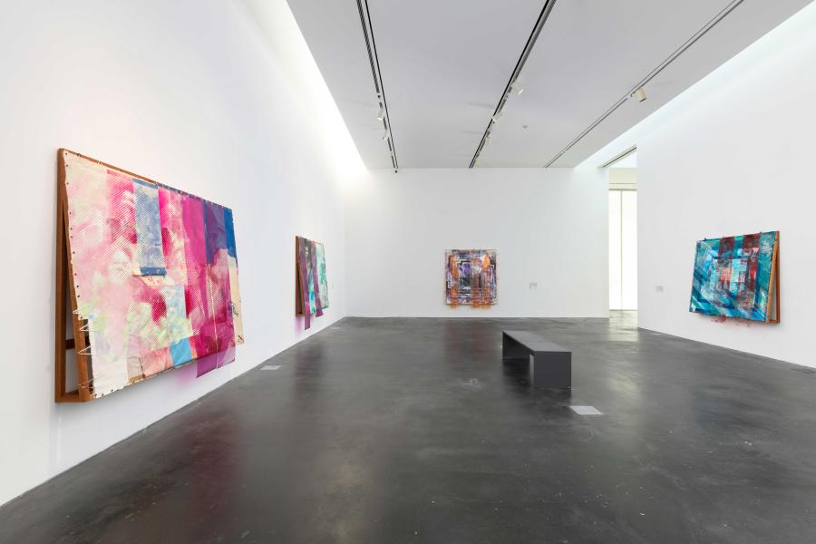 Four large abstract artworks hung on white walls in an MCA Denver gallery. There is a bench in the center of the room.