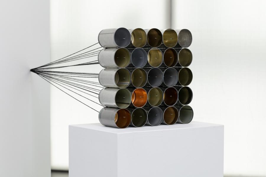 Tin cans stacked on top of one another, positioned on a white pedestal in an MCA Denver gallery.