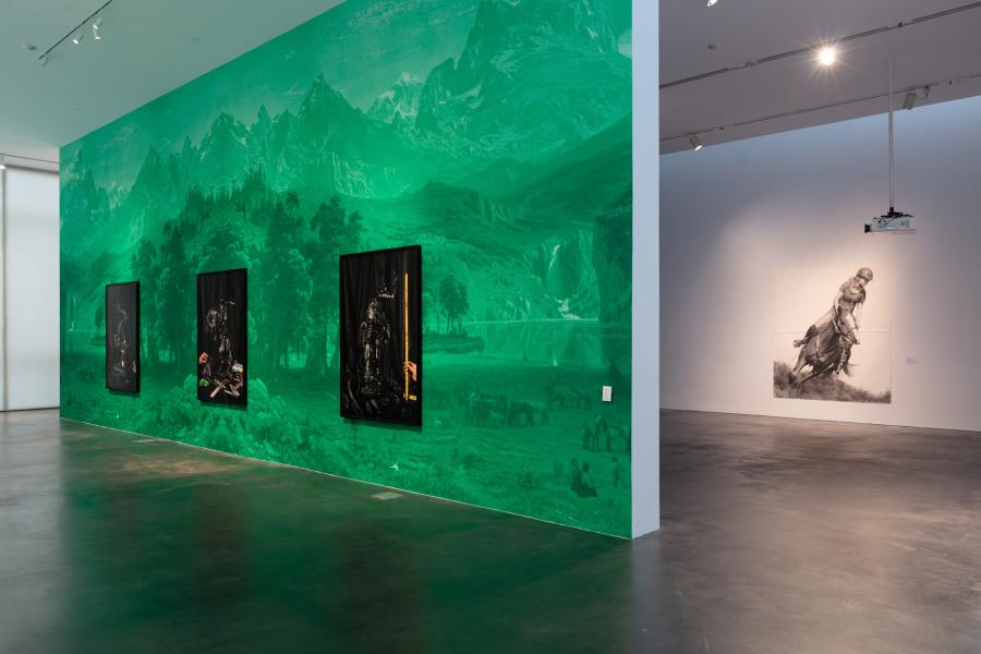 Gallery featuring large framed artwork on a wall wrapped in a green landscape vinyl. In view is another gallery with a huge drawing of a girl on a horse.