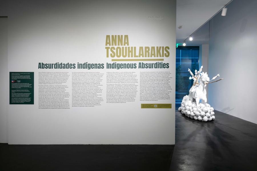 Wall text that reads, "Anna Tsouhlarakis: Indigenous Absurdities". There is a large white plaster horse in view next to the wall text. 