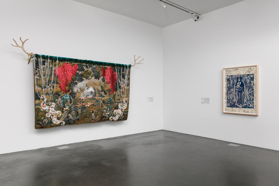Corner of an MCA Denver gallery displaying two artworks on the wall. One is large and has antlers coming out of it, the other shows a figure in blue.