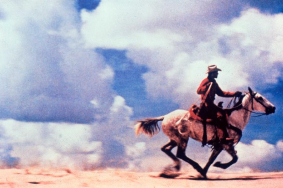 Print featuring a cowboy riding a horse in front of a bright but cloud filled blue sky.