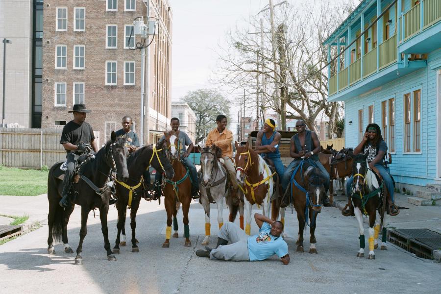 Image of seven people on horseback, all standing in the street. There is one person laying on the street in front of the horses. 