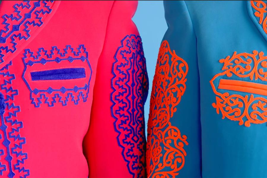 Still from a video featuring a closeup of two people standing side by side in colorful embroidered jackets.
