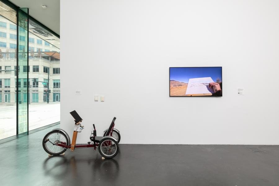 Gallery featuring a small bike next to a small television displaying a video.