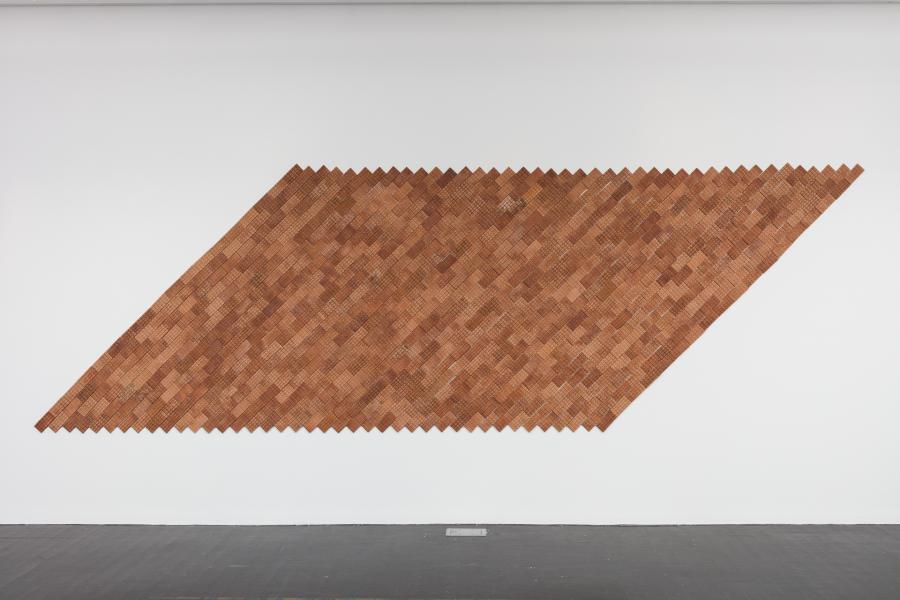 Brown artwork on a gallery wall that looks like a slanted rectangle.