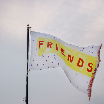 A white flag with purple dots flying in the air, with the word "friends" on it in all caps in the color red.