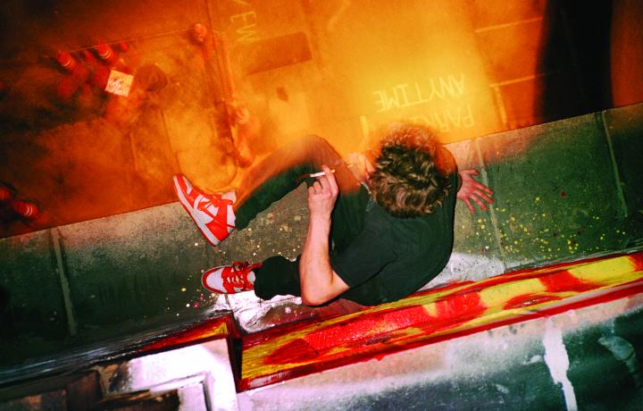 Photograph by Ryan McGinley of a man from above. He is sitting on a dirty ledge overlooking a street while smoking a cigarette.