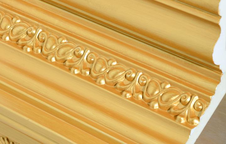 Detail shot of wall trim covered in fake gold. The inside is exposed revealing it is actually a cheap and gaudy material