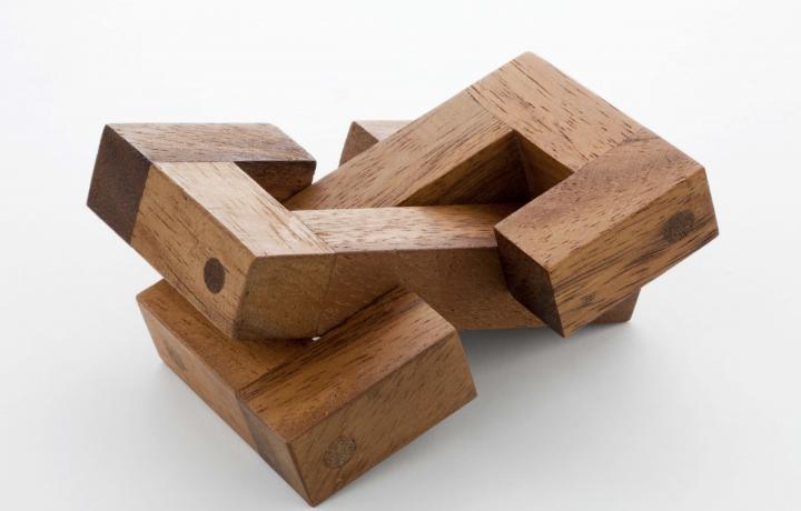 Two blocks of wood cut into two “C” shapes entangle each other against a white background. 