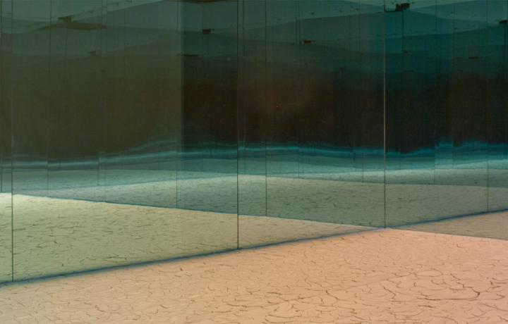 Installation shot in an unknown space. Large mirrors make up the walls creating a sense of infinity. Cracked tan sand makes up the floor. 