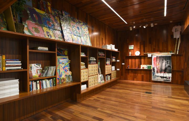 An interior room with wooden walls, ceiling, and flooring. There are various archival materials on wooden shelves including books, and salvaged walls. 