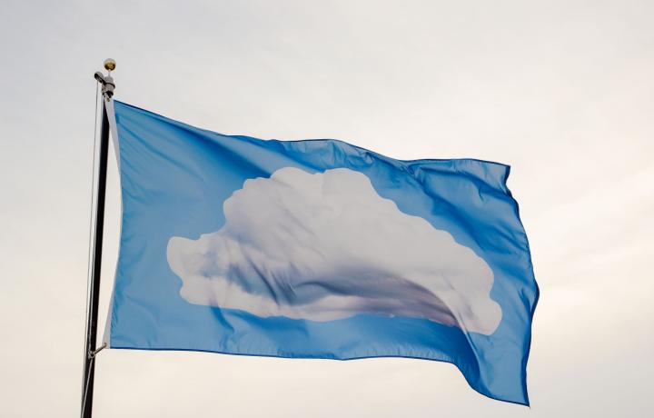  A cerulean flag with an image of a fluffy cotton-white cloud flies against an overcast sky.