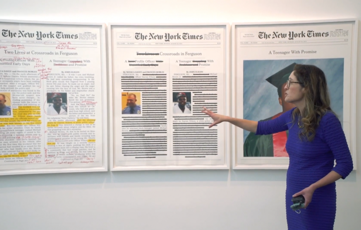 Image of Miranda Lash in a gallery standing in front of artist Alexandra Bell's work hung on a white wall in one of the MCA Denver galleries. The work is a framed triptych with annotations of front-page layouts of the headlines in the NYT that report on the murder of Michael Brown.