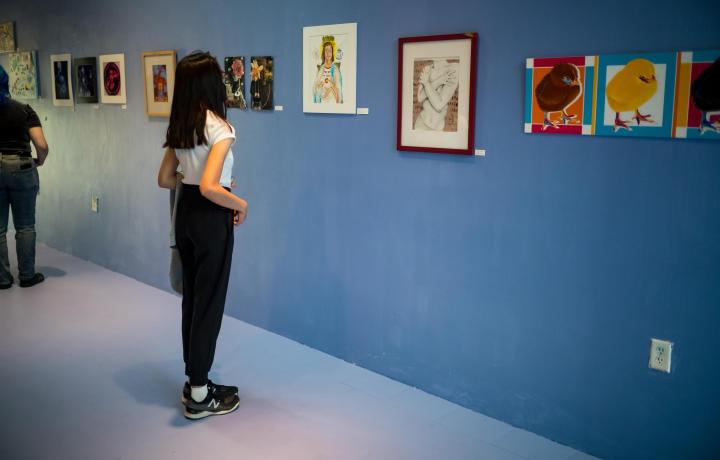 Person standing in MCA Denver teen exhibition space, looking at artwork hung on a blue wall. 