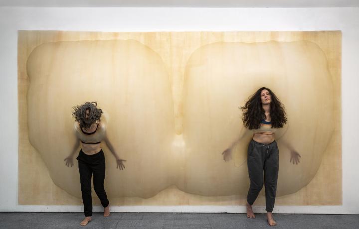 Performance featuring two people bumping up against a breast-like installation in a gallery.