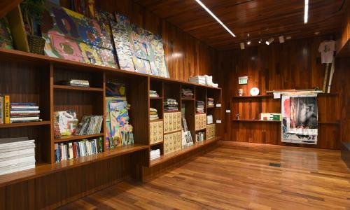 An interior room with wooden walls, ceiling, and flooring. There are various archival materials on wooden shelves including books, and salvaged walls. 