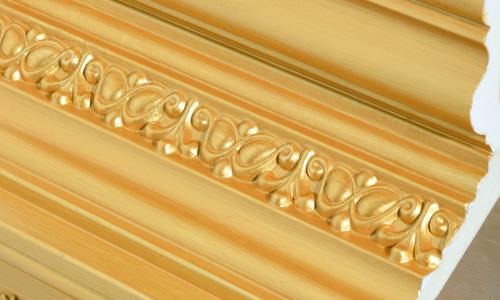 Detail shot of wall trim covered in fake gold. The inside is exposed revealing it is actually a cheap and gaudy material