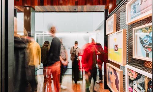 Several people view artwork in a gallery. The shutter speed was low resulting in an image that evokes movement