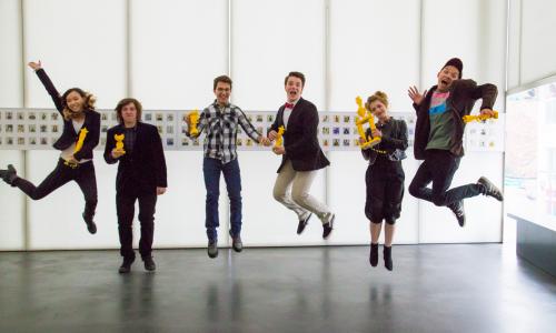 Young adults mid jump holding yellow trophies