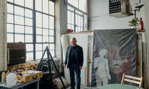 Portrait of Clark Richert standing in a gallery space. There are large canvasses behind him. 