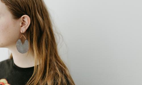 A young woman models gray earrings that resemble a pie chart. 