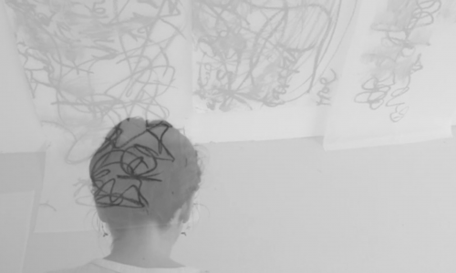 Black and white abstract moody image of the back of an individual’s head, their hair is up and only their head and neck are in view. Another somewhat unidentifiable image—perhaps a work of art by the artist— is superimposed on top and looks like scribbles. 
