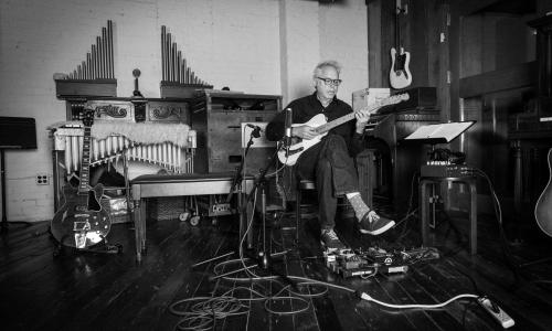black and white image of Bill Frisell in his studio with instruments all around him