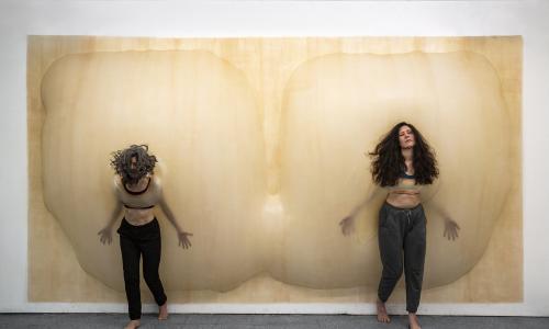 Performance featuring two people bumping up against a breast-like installation in a gallery.