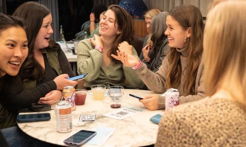 People laughing and crafting in a cafe, sitting around a table.