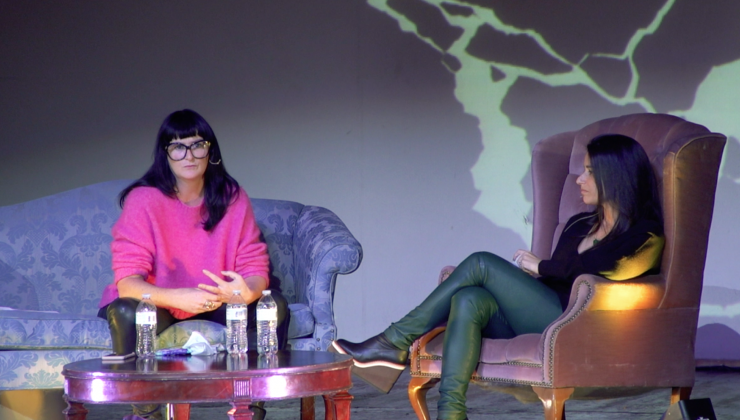 Tara Donovan and Nora Burnett Abrams sit on two armchairs on a stage. In front of them is a wooden coffee table with water bottles.